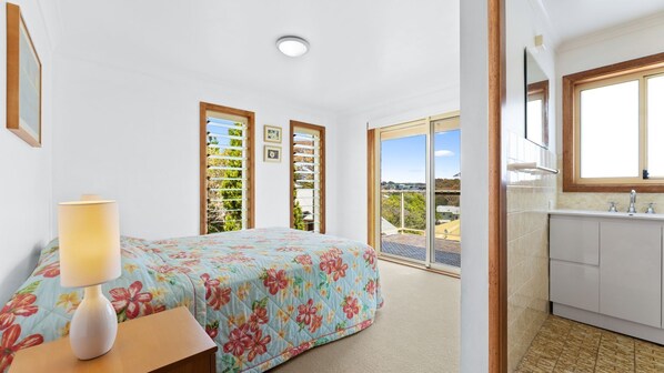 A bedroom with a bed, a nightstand, a lamp, a window with blinds, and a view of the outside.