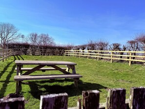 A picnic table in a grassy area with a wooden fence and trees in the background. - Pond Cottage (Alnwick)