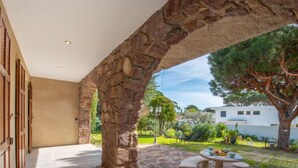 A stone archway leading to a patio with a stone table and chairs, surrounded by greenery and a white building in the background. - Le Jasmin by Interhome (Cavalaire)