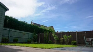 En bostadsträdgård med ett växthus, ett trästaket och en stenlagd uteplats.