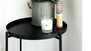 En krukväxt med stora, gröna blad står på ett svart bord bredvid ett ljus och en dekorativ prydnad.