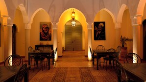 A dining area with tables and chairs, a chandelier, and a door in the background. - Villa Agora (Sidi Abdallah Ghiat)
