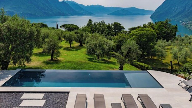 En modern infinitypool med fri utsikt över en sjö och berg.