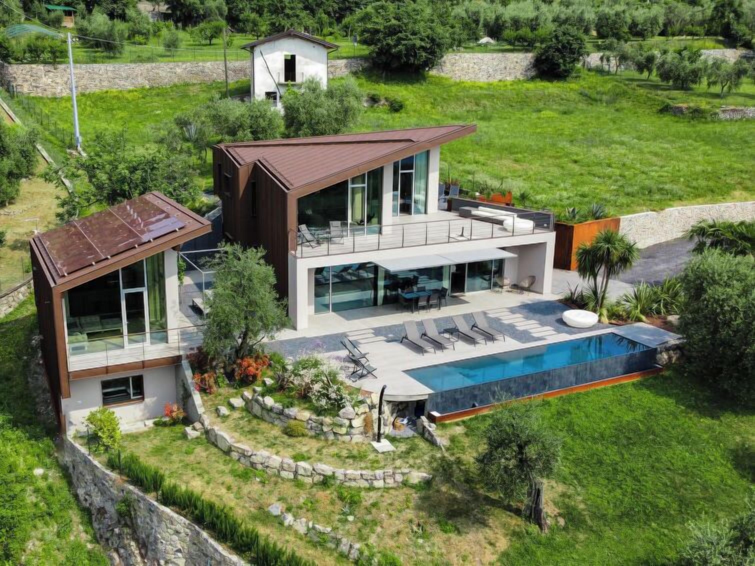 Une maison moderne à deux étages, dotée d’une grande façade vitrée, d’une piscine et d’un mur de soutènement en pierre.