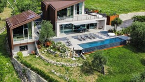 Ett modernt hus i två v åningar med en stor glasfasad, en swimmingpool och en mur av sten som fungerar som stödmur.