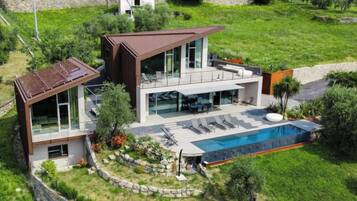 Une maison moderne à deux étages, dotée d’une grande façade vitrée, d’une piscine et d’un mur de soutènement en pierre.