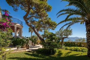 Eine Villa im mediterranen Stil mit Balkon, üppigem Grün und Blick aufs Meer.