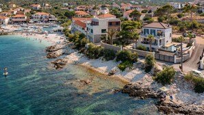 A coastal town with a beach, houses, and a large building with a pool.