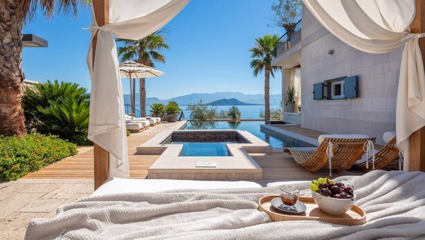 A luxurious outdoor pool area with a view of the sea, a wooden deck, and lounge chairs.