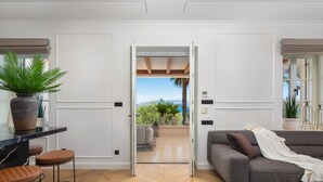 A modern interior with a dining area, a sofa, and a view through an open door to an outdoor patio.