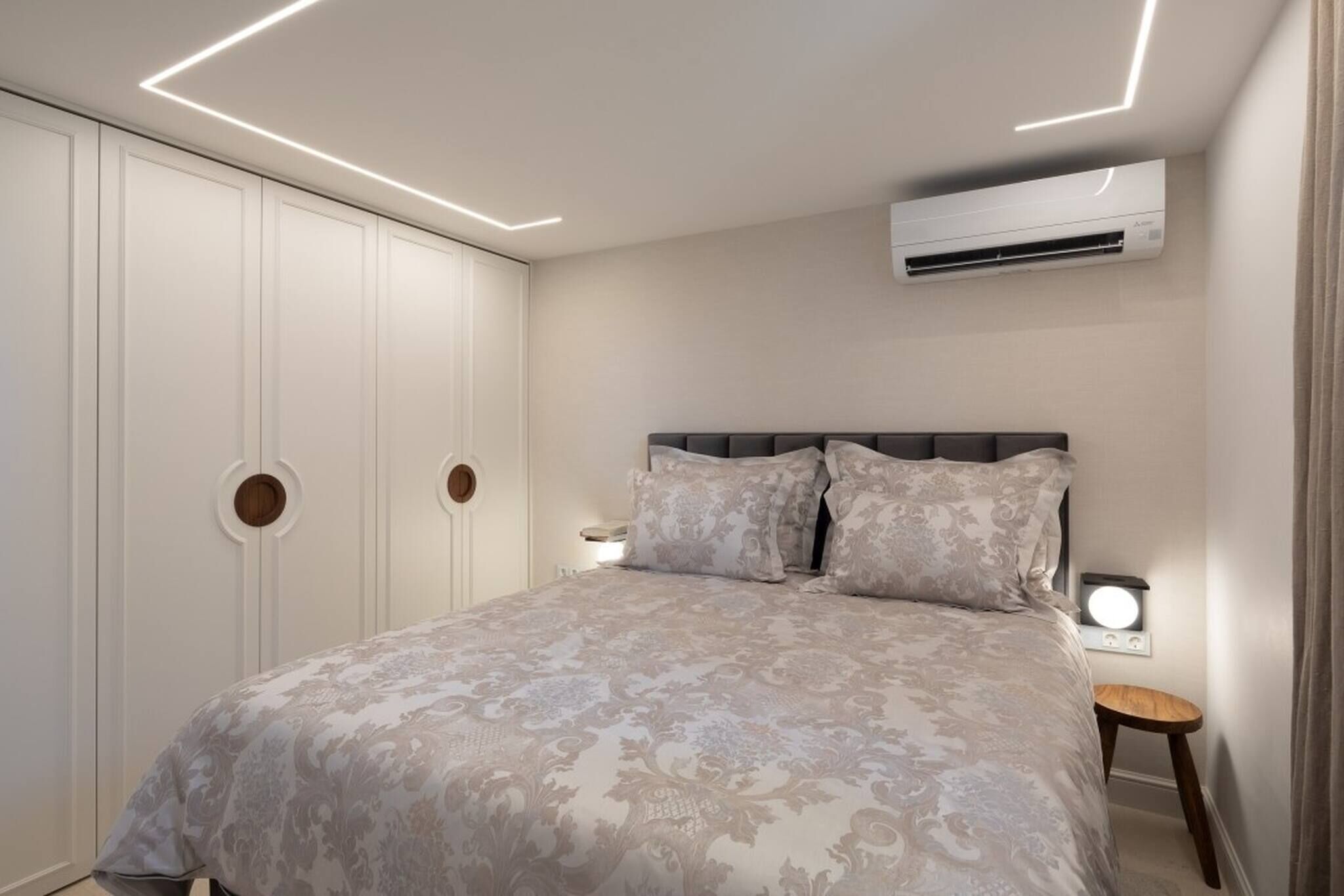 A bedroom with a bed, bedside lamps, an air conditioning unit, and a wardrobe.