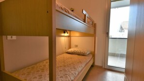 A small, compact room with a bunk bed and a single bed. There is a door leading to a balcony with a view of the outside. - Stefania by Interhome (Aprica)