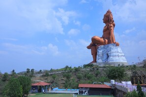 A large statue of a seated figure on a pedestal, surrounded by greenery and a clear sky. - Shiv Ashray Resort (Nathdwara)