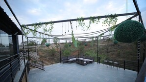 An outdoor patio with a seating area, a staircase, and a view of the surrounding landscape. - Shiv Ashray Resort (Nathdwara)