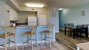 Una cocina con barra, sillas de madera, una mesa de comedor y un reloj en la pared.