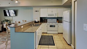 Una cocina moderna con gabinetes blancos, encimera de granito, horno integrado, microondas y refrigerador.