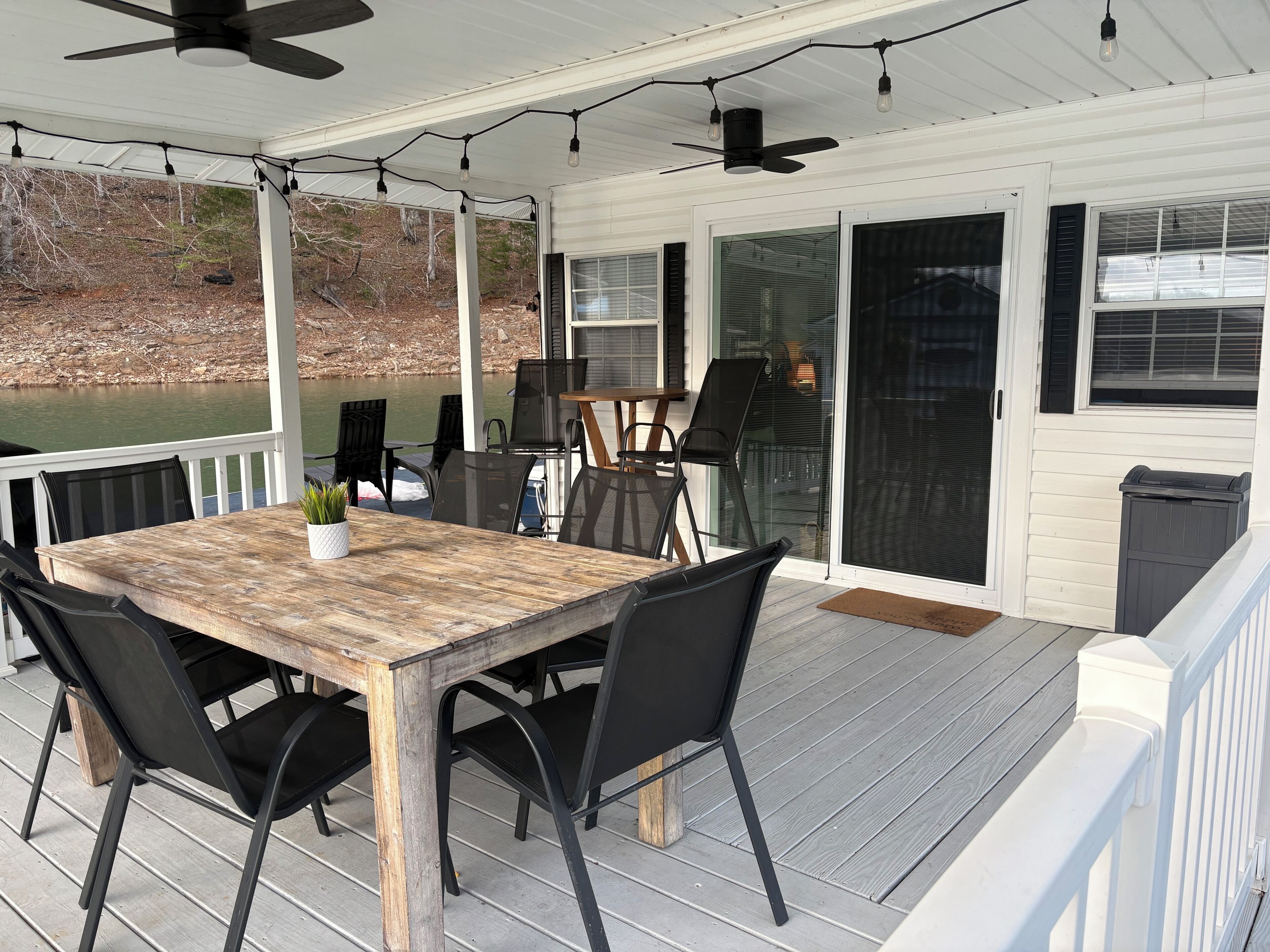 A covered deck with a table and chairs, a ceiling fan, and a view of a body of water.