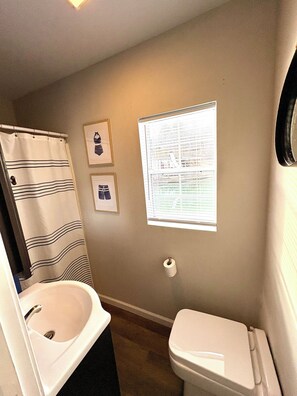A bathroom with a toilet, a sink, a shower curtain, and a window with blinds.