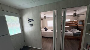 A room with a bunk bed, a ceiling fan, a window with blinds, and a door leading to another room. - Floating Cabin - Another Day in Paradise at Whitman Hollow Marina (LaFollette)