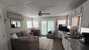 A spacious living area with a sofa, a television, and a kitchen area with a sink and cabinets. - Floating Cabin - Another Day in Paradise at Whitman Hollow Marina (LaFollette)