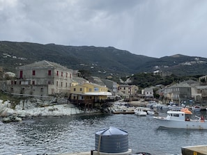 A coastal village with traditional buildings, a harbor with boats, and a mountainous backdrop.