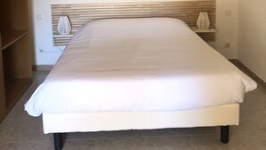 A bedroom with a bed, wooden headboard, bedside table, lamp, and a wall-mounted air conditioner. - Holiday residences 5 minutes from the beach (Centuri)