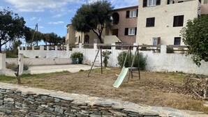 A residential area with a stone wall, a swing set, and a building with multiple windows and balconies. - Holiday residences 5 minutes from the beach (Centuri)