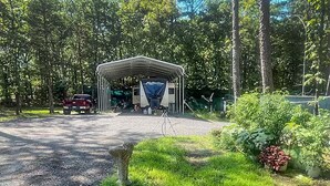 Un espace extérieur abrité, avec un chemin de gravier menant à un bâtiment, le tout entouré d’arbres et de verdure.