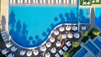 Ett flygbildsbild av ett semesterområde med en stor pool i mitten, flera mindre pooler och ett stort antal solstolar placerade runt poolområdet.