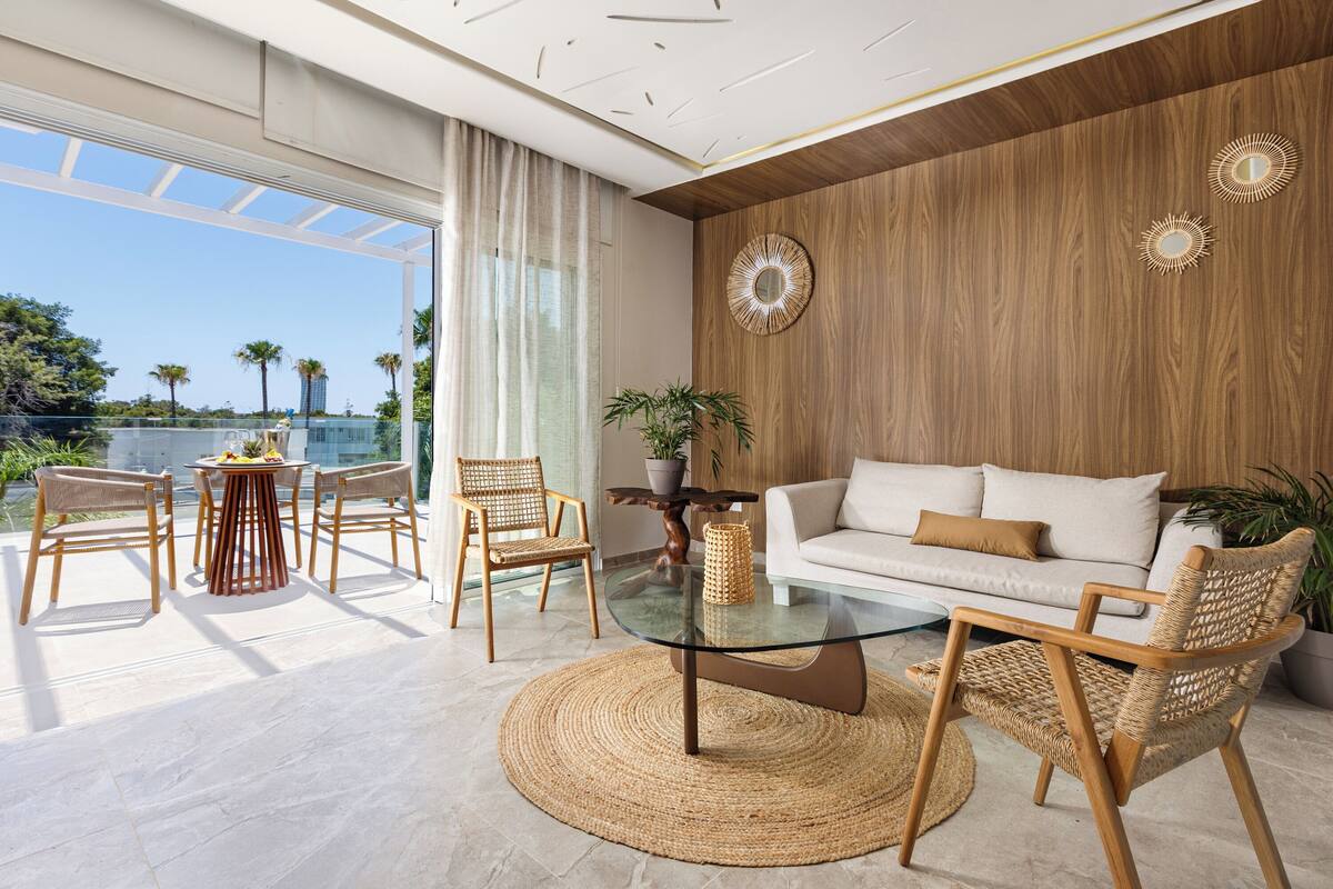 A modern living room with a glass coffee table, wicker chairs, a white sofa, and a wooden accent wall.