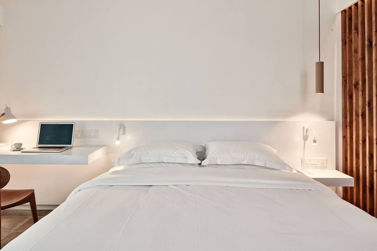 A modern bedroom with a bed, a desk with a laptop, and a wooden accent wall.
