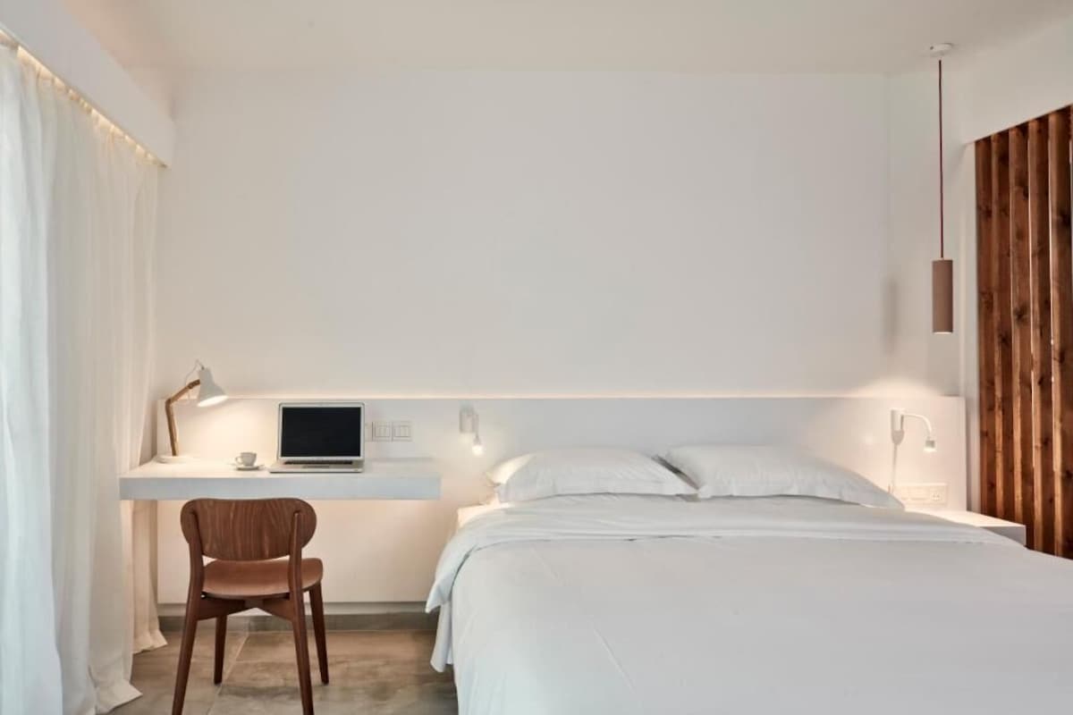 A bedroom with a bed, a desk with a laptop, a chair, and a bedside table.