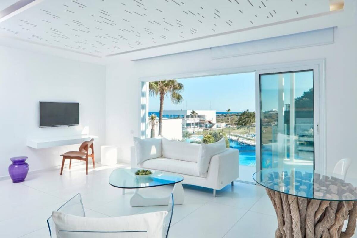 A modern living room with a white sofa, a glass coffee table, and a TV mounted on the wall.