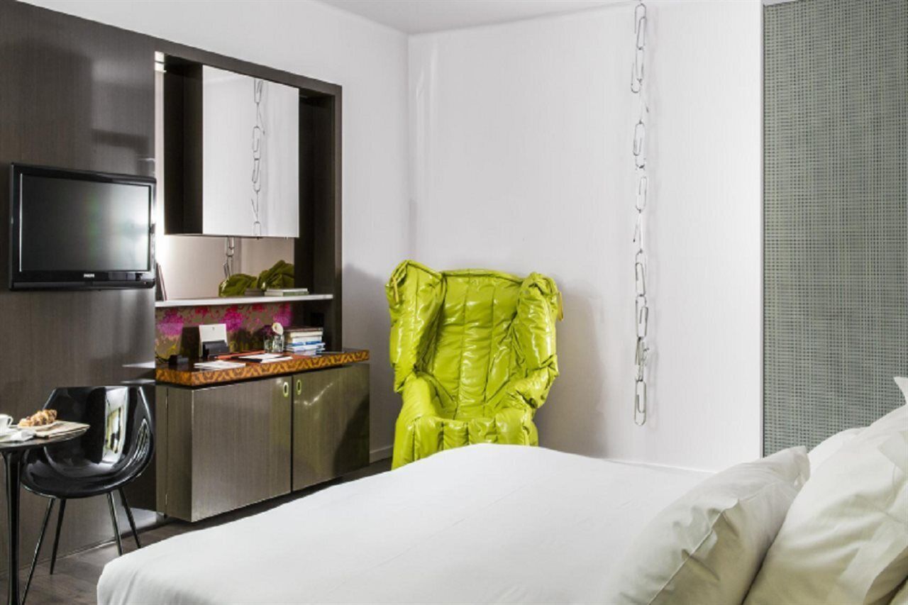 Een hotelkamer met een bed, een bureau met een computer, een televisie en een felgroene stoel.