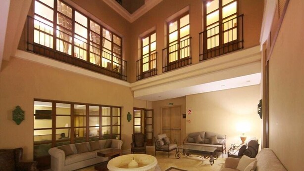 A spacious living area with multiple seating options, including sofas and armchairs, arranged around a central coffee table. Large windows with balconies provide natural light and views. - Hotel Casa Consistorial (Fuengirola)