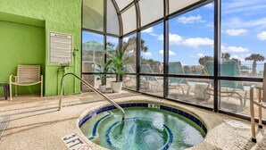 An indoor swimming pool with a view of the sky and palm trees, surrounded by lounge chairs and a green wall. - Penthouse Suite/ Oceanfront/Prime location (Myrtle Beach)