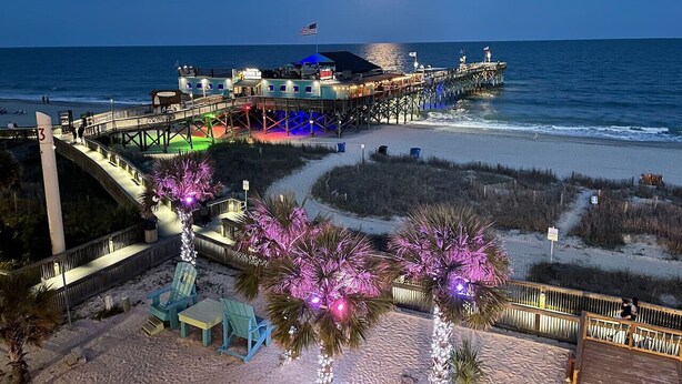 A pier extending into the ocean with a building at the end, a walkway, and palm trees with lights. - Penthouse Suite/ Oceanfront/Prime location (Myrtle Beach)