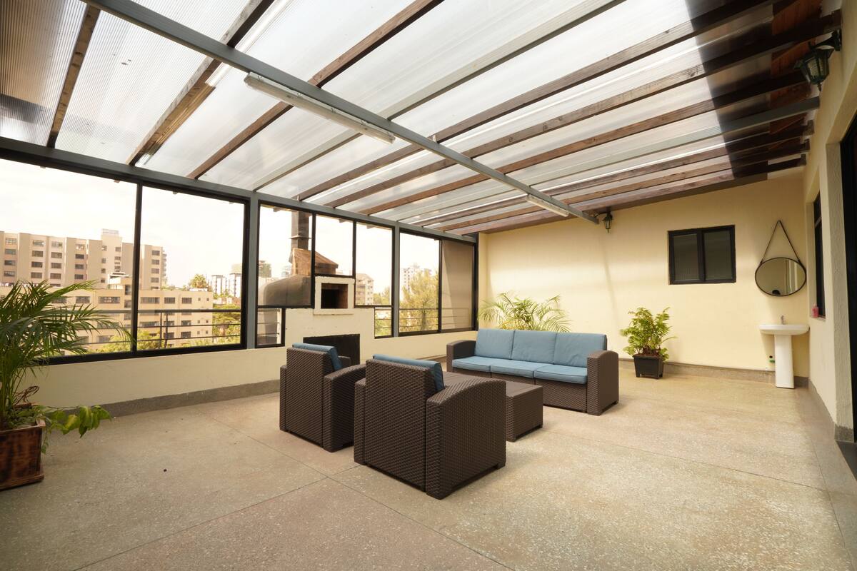 A spacious balcony with a glass ceiling, wicker furniture, a blue sofa, and potted plants.