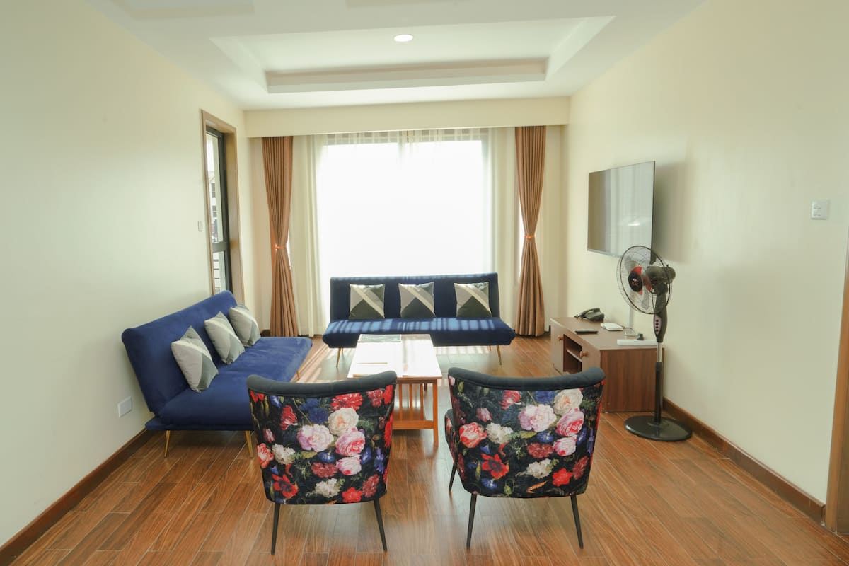 A living room with a sofa, two chairs, a coffee table, a TV, and a fan.