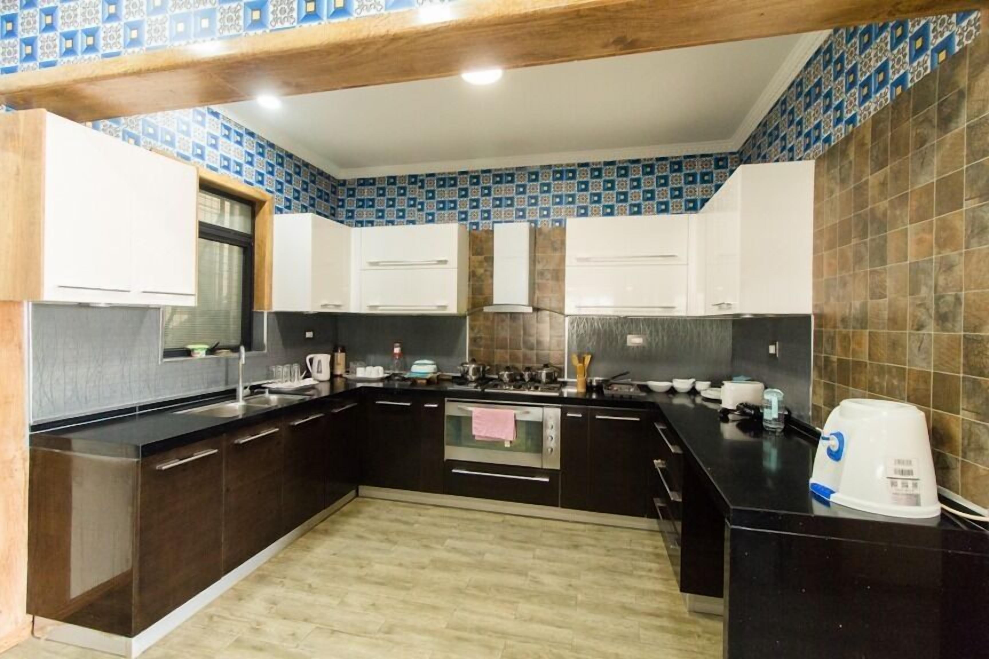A kitchen with dark cabinetry, a black countertop, and patterned backsplash.