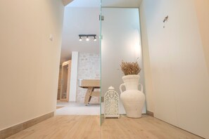 Spacious room with a clear glass partition, a bench, and a decorative vase with plants.