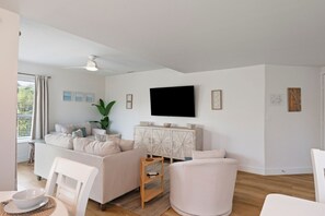 Un salon moderne comprenant un canapé, des fauteuils, un téléviseur et un meuble.