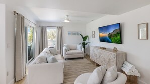 Een moderne woonkamer met een zithoek, een televisie en een groot raam met gordijnen.