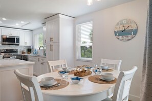 Une cuisine moderne avec des meubles blancs, un îlot central et un coin repas comprenant des chaises blanches et une table ronde.