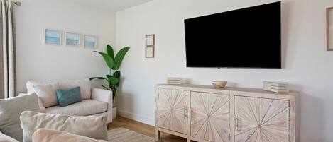 Una sala de estar con sofá, planta, aparador y televisor.