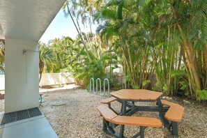 Une terrasse extérieure avec une table et des bancs en bois, entourée de palmiers et recouverte de gravier.