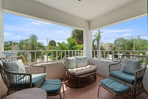 Een balkon met rieten meubilair en uitzicht op palmbomen en huizen.