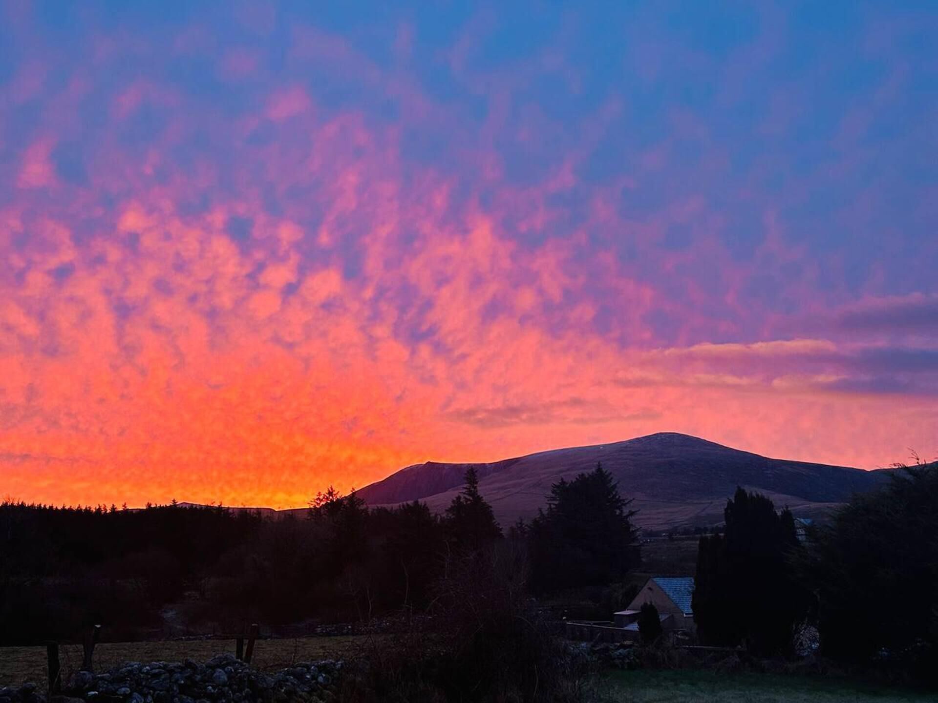 A mountain landscape at sunset with a house in the foreground.