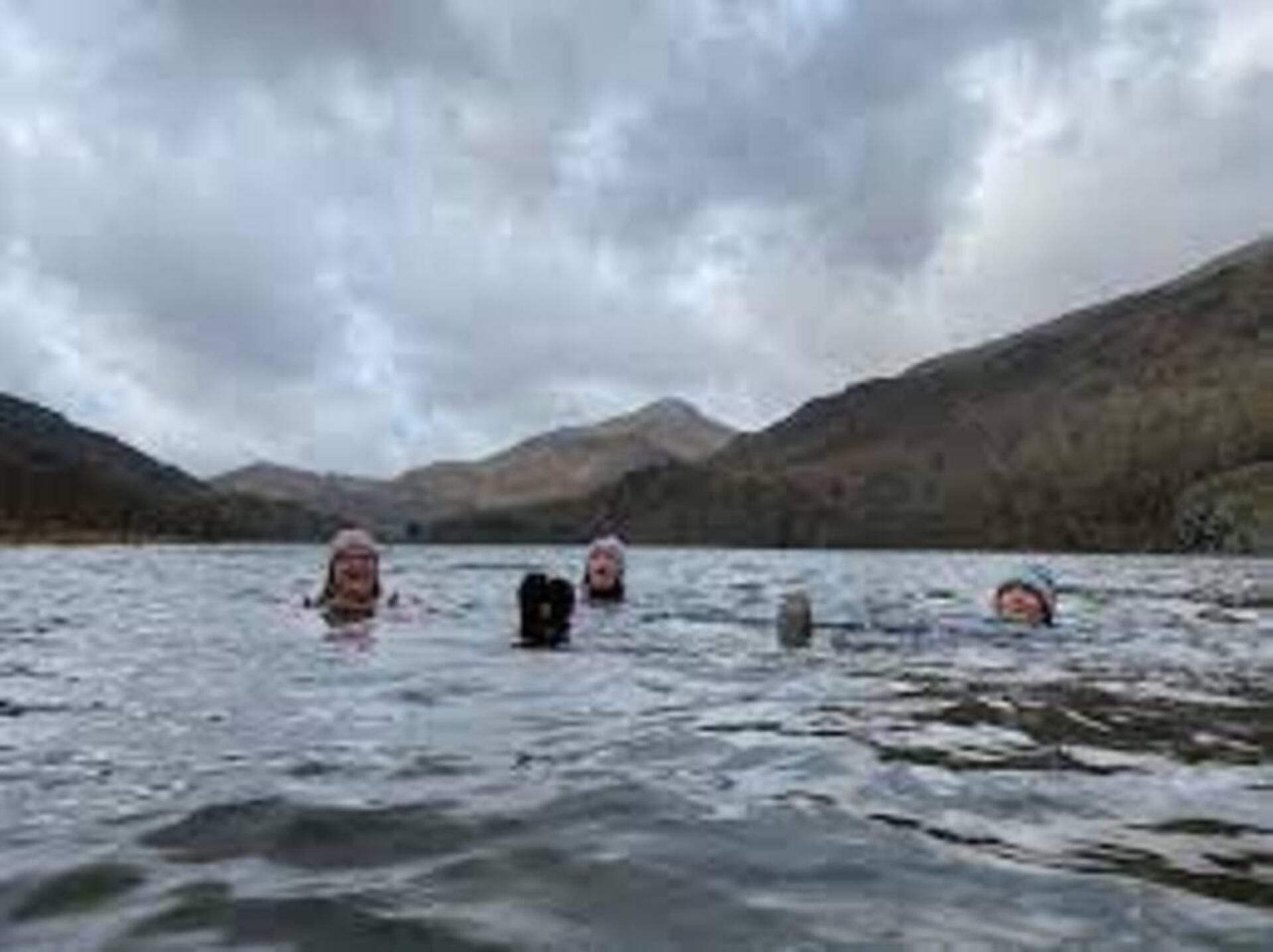 Eine Gruppe von Menschen schwimmt in einem See, der von Bergen umgeben ist.