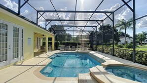 Une piscine dotée d’une zone abritée et de chaises longues, entourée d’une clôture et de verdure.
